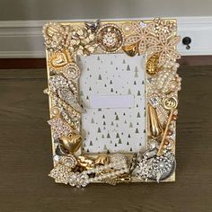 a gold and white photo frame with pearls, jewels and other things in it on a wooden table