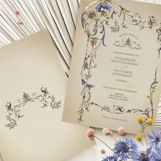 two wedding cards on top of each other next to blue flowers and fanned fans