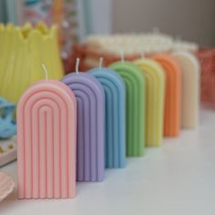 a row of candles sitting next to each other on a white table with different colors