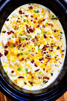 a crock pot filled with cheese, bacon and other toppings on top of a wooden table