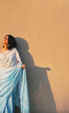 a woman in a blue and white dress leaning against a wall