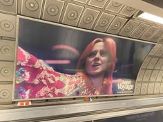 a billboard on the side of an escalator in a subway station, featuring a woman with red hair