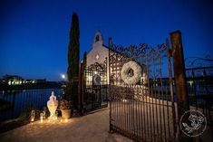 an iron gate with candles surrounding it and a building in the background at night time