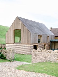 a wooden house sitting on top of a lush green field next to a stone wall