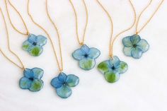 four blue and green flower necklaces on a white surface with two gold chains hanging from them