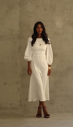 a woman standing in front of a wall wearing a white dress