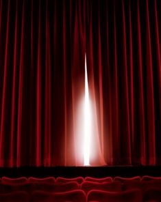 an empty theater stage with red curtains and the light coming from behind it in front of a window