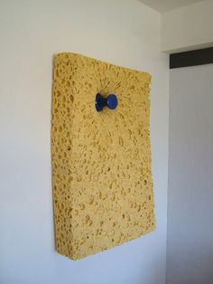 a yellow sponge is hanging on the wall with a blue plastic object attached to it