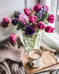 a cup of coffee sits on a book next to a bouquet of tulips