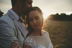 a bride and groom embracing each other in an open field with the sun behind them