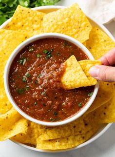 a hand dipping tortilla chips into a bowl of salsa