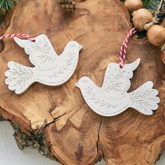 two white doves with red and white striped twine on them sitting on a piece of wood