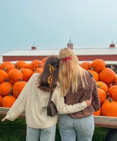 two women standing next to each other in front of a truck full of pumpkins