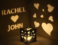 a lit up cube sitting on top of a table next to two cut out hearts