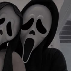 two people wearing masks with faces painted black and white, one is holding the other's head