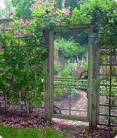 an open gate in the middle of a garden with pink flowers growing on it's sides