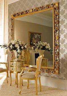 a mirror sitting on top of a wall next to a table with flowers in it