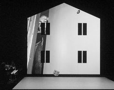 a man standing on top of a stage next to a white building with black windows