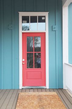 a red door is on the side of a teal blue house with wood flooring