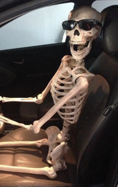 a skeleton sitting in the driver's seat of a car, with sunglasses on