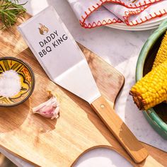 a wooden cutting board topped with corn on the cob next to a spatula