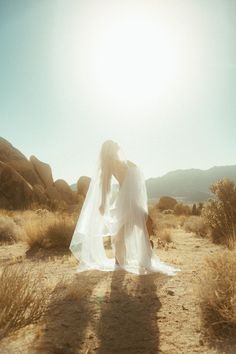 a woman in a white wedding dress is standing in the desert with her veil over her head