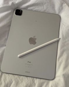 an apple ipad with a pencil on it sitting on top of a white bed sheet