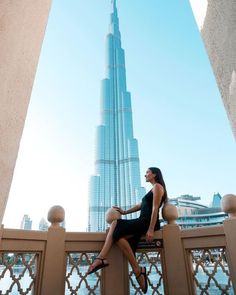 a woman sitting on top of a fence next to a tall building