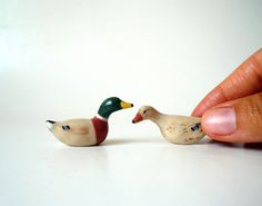 two small wooden ducks sitting next to each other on a white counter top in front of a person's hand