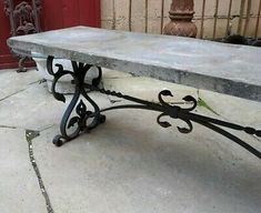 an iron bench sitting on top of a cement floor next to a red door and brick wall