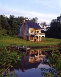 a white house sitting on top of a lush green field next to a body of water