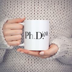 a woman holding a white coffee mug with the word ph dva in black on it