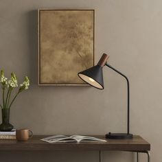 a desk lamp sitting on top of a wooden table next to a vase with flowers