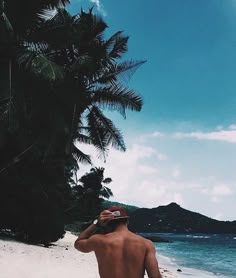 the man is walking on the beach talking on his cell phone while wearing a hat