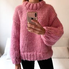 a woman in a pink sweater taking a selfie with her cell phone while standing on a white couch