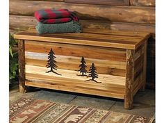 a wooden chest with pine trees painted on the front and sides, sitting next to a pile of blankets