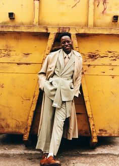 a man in a suit leaning against a yellow dumpster