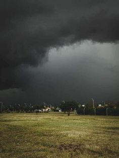 a large field that has some grass in it and dark clouds above the fields behind it