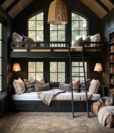 a bunk bed with lots of pillows and blankets on it in front of two windows