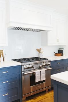 a stove top oven sitting inside of a kitchen next to blue cabinets and white counter tops