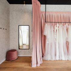 pink and white wedding gowns hanging in front of a mirror on the wall next to a bench