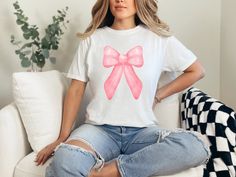 Indulge in the perfect gift for Mom with a trendy coquette pink bow aesthetic on her birthday or for Mother's Day - our Comfort Colors T-shirts.  Crafted from the finest 100% ring-spun USA cotton, these shirts offer unmatched comfort with a medium weight, pre-shrunk fabric.  Our ethically grown and harvested cotton ensures not just a soft touch but also a clear conscience.  The garment-dyed, soft-washed fabric brings an extra layer of coziness to their wardrobe, making these tees an ideal daily choice.  The relaxed fit offers both style and comfort, while the double-needle stitching ensures durability that stands the test of time.  Say goodbye to side-seams as our tubular-shaped shirts maintain their form effortlessly.  Elevate gifting with the perfect blend of quality, style, and personal Trendy Pink T-shirt For Birthday, Trendy Pink Tops For Birthday, Cute Pink T-shirt With Bow, Pink Tops With Bow For Party, Pink Party Top With Bow, Cute Party Tops With Bow, Cute Party Tops With Bow Detail, Pink Casual T-shirt For Party, Casual Pink Party T-shirt