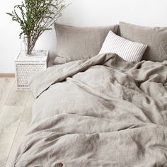 an unmade bed with two pillows and a plant in a basket next to it