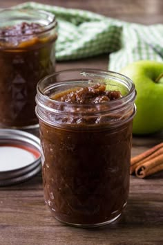 two jars filled with apple chut next to cinnamon sticks and an apple in the background