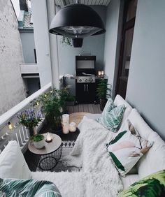 an apartment balcony with white and green pillows on the couches, potted plants and a grill in the background