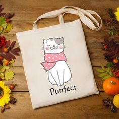 a tote bag with a cat on it sitting next to autumn leaves and pumpkins