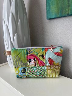 a white vase sitting on top of a table next to a small purse filled with colorful fabric