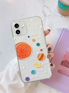 a woman holding up her phone case with the planets on it next to a book