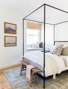 a bedroom with a four poster bed and white walls, hardwood flooring and artwork on the wall