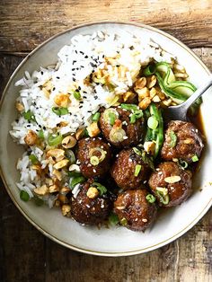 a white plate topped with meatballs and rice on top of a wooden table next to a fork